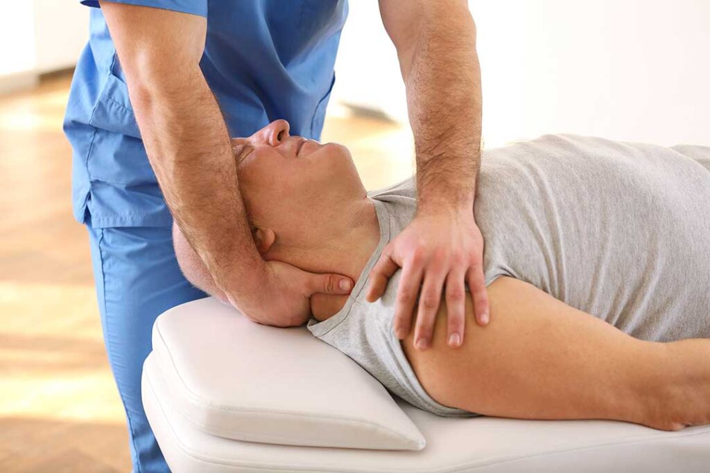 Person performing gentle shoulder mobility exercises beside a chair in a bright home.