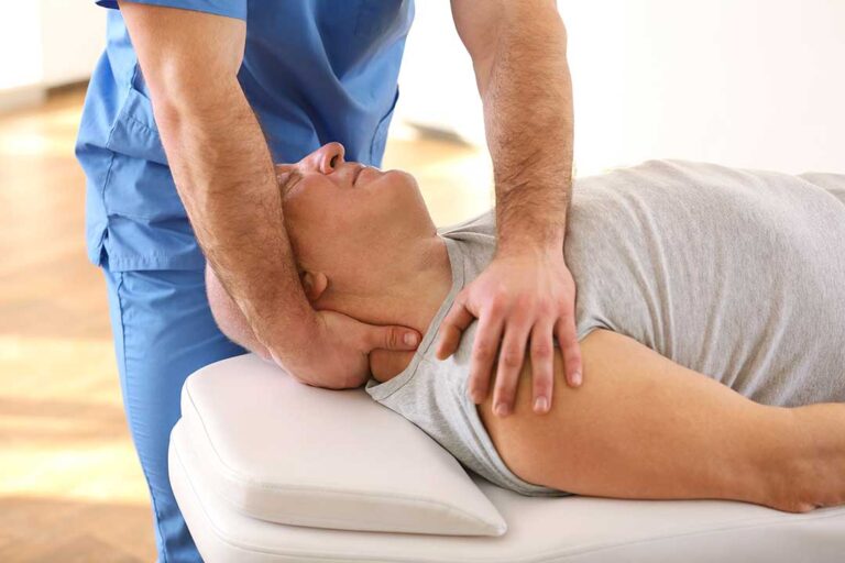 Person performing gentle shoulder mobility exercises beside a chair in a bright home.