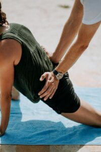 Adult practicing a guided back stretch on a mat beside a clinician in a bright wellness room.