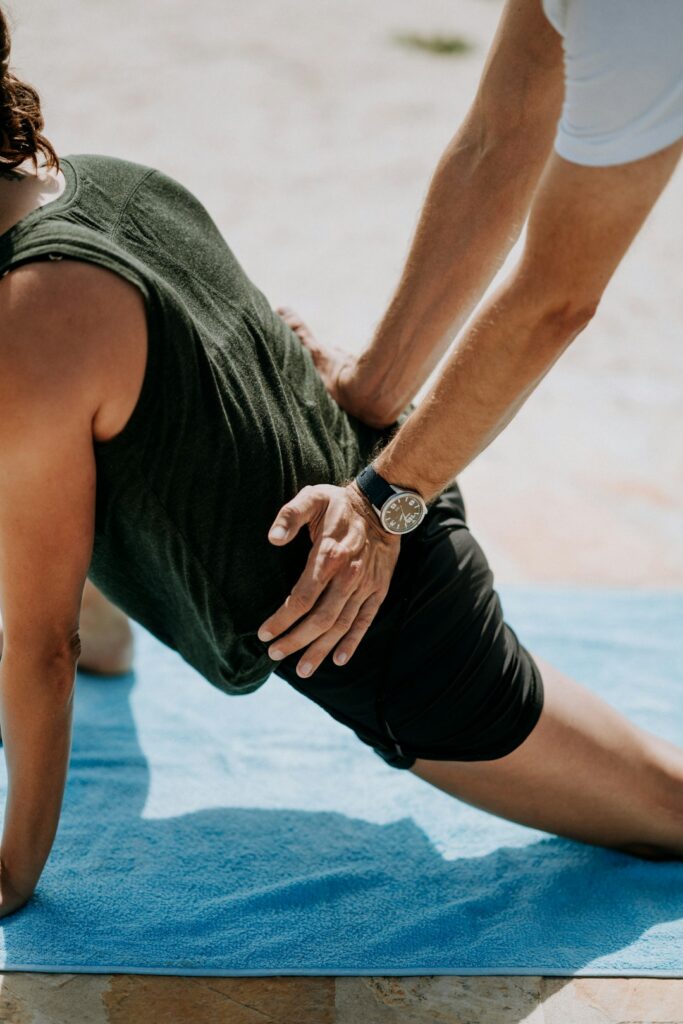 Adult practicing a guided back stretch on a mat beside a clinician in a bright wellness room.